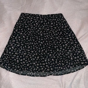 Svart blommig kjol från H&M Divided - Söt lågmidjad svart kjol från H&M Divided med ljusa blommor. Det är en kortkjol fast som täcker tillräckligt och är perfekt till sommaren. 