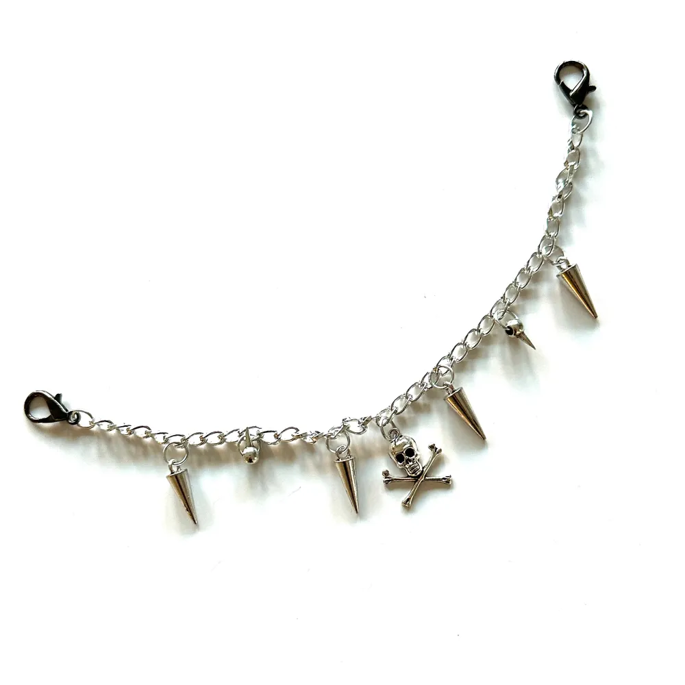 Coolt silverfärgat accessoarsmycke med hängande dödskalle och spikar. Sätt på väskan, bältet eller byxorna för att få en unik touch på din look. 🤟⭐️. Asusteet.