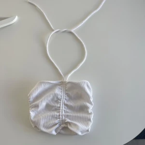 Vit ribbad bandeau topp med knyte  - En vit ribbad bandeau topp med knyte runt halsen, går att justera längden på den genom banden. Aldrig använd! Lite genomskinlig 