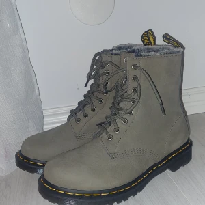 Grå boots med foder - Snygga grå boots från Dr. Martens med snörning och mjukt foder. De har den klassiska gula sömmen och en robust sula som ger bra grepp. Perfekta för kyligare dagar. Är storlek 41 men skulle lika gärna kunna passa 39 och 40 också.