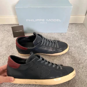 Philippe models low - Snygga svarta sneakers från Philippe Model med mörkröda detaljer vid hälen. Skorna har en klassisk design med snörning och en vit sula som ger en stilren look. Perfekta för en avslappnad stil.