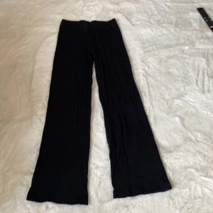 Svarta ribbade byxor - Snygga svarta byxor med ribbad struktur och vid passform. Perfekta för en avslappnad stil. De har en hög midja och är tillverkade i ett mjukt material som ger en bekväm känsla.