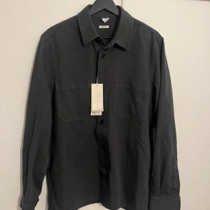 Overshirt från Arket - Snygg overshirt från Arket med klassisk krage och knappar framtill. Skjortan har två bröstfickor och en stilren design som passar perfekt för en modern look.