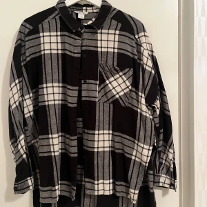 Svart och vit rutig skjorta från Monki - Snygg svart och vit rutig skjorta från Monki i storlek S. Skjortan har långa ärmar och en klassisk krage. Perfekt för en avslappnad stil med en bröstficka som extra detalj. Passar bra till jeans eller kjol för en cool look.