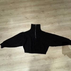 Svart stickad polotröja från Gina Tricot - Säljer en svart stickad polotröja från Gina Tricot med dragkedja framtill. Tröjan har en hög krage och långa ärmar, perfekt för kyligare dagar. Den är både stilren och bekväm. Tröjan är kroppad och sitter snyggt