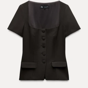 Mörkbrun kortärmad blus från Zara - Elegant blus från Zara med korta ärmar och fyrkantig urringning. Blusen har knappar framtill och dekorativa fickdetaljer. Perfekt för en stilren look.