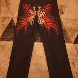 Svarta byxor med broderi - Snygga svarta byxor med ett coolt rött och vitt broderi på baksidan. Byxorna har en rak passform och är perfekta för att ge en unik touch till din outfit.