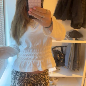 Vit blus med volangdetaljer - Säljer en söt vit blus med volangdetaljer och smockad midja!