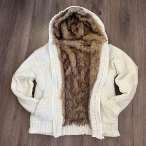 Vit stickad cardigan med päls - Säljer en vit stickad cardigan med huva. Storlek L, modellen är 176. Passar klockrent på någon som är 180+ Fodrad med päls hela insidan förutom armarna som är quiltade. Bvsa, hör av dig vid frågor.