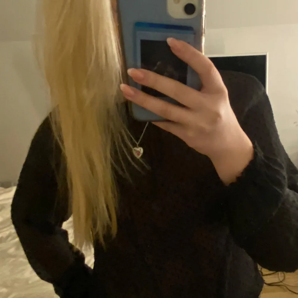 Säljer en elegant svart blus med diskret prickigt mönster. Blusen har långa ärmar och en lös passform, perfekt för en stilren look. Den är tillverkad i ett lätt och luftigt material.. Neuletakit & Villapaidat.
