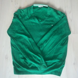 Grön tröja från J.Lindeberg - Säljer en snygg grön tröja från J.Lindeberg med v-ringning och diskret logga på bröstet. Perfekt för en stilren look och till golfen. Tröjan har långa ärmar och är tillverkad i ett mjukt material. Skriver storlek L / M för den passar som de