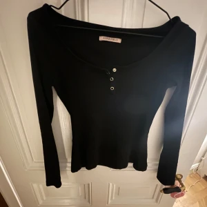 Svart långärmad topp från Anna Field - Snygg svart långärmad topp från Anna Field med rund halsringning och tre dekorativa knappar framtill. Perfekt för en stilren look. Står ingen storlek men skulle gissa på xs/s.
