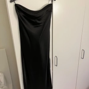 Svart axelbandslös klänning - PRIS DISKUTERAS!! 🤗💗Elegant svart axelbandslös klänning i satin med en snygg passform. Har en knytning i ryggen som gör det ganska öppet i ryggen, och en stilren design som passar perfekt för festliga tillfällen. Använd endast 1 gång vid ett julfirande!