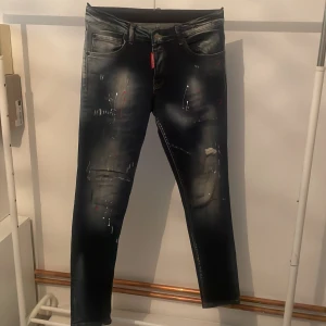 Svarta jeans från Dsquared2 - Snygga svarta jeans från Dsquared2 med coola slitningar och färgstänk. De har en klassisk femficksdesign och en röd etikett vid gylfen. Perfekta för en trendig look och ett litet hål i fickan, dm mig om stroleken 