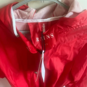 Röd regnjacka från Rains - Ascool röd regnjacka från Rains med knappar och knytband i midjan. Den är perfekt för regniga dagar🌧️🫶🏻Aldrig använd då jag har fler regnjackor. Säljer för 350kr + frakt 