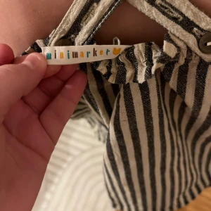 Randig topp från Mini Market - Säljer en randig topp från Mini Market med smala axelband som korsas i ryggen. Toppen har ett avslappnat och luftigt snitt, perfekt för varma dagar. Den är i en klassisk svart och beige färgkombination.