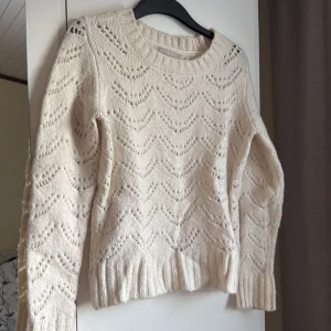 Beige stickad tröja - Mysig beige stickad tröja från Pieces med ett vackert hålmönster. Tröjan har långa ärmar och ribbade kanter vid hals, ärmslut och nederkant. Perfekt för kyliga dagar!