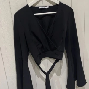 Svart topp från NaKd - Snygg svart omlottopp från NA-KD med långa ärmar och knyte bak till ryggen