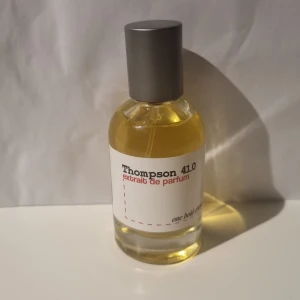 Thompson 41.0 Extrait de Parfum - Elegant flaska med Thompson 41.0 Extrait de Parfum. Parfymen har en stilren design med en genomskinlig glasflaska och en grå kork. Etiketten är vit med röd och svart text. Perfekt för den som söker en unik doftupplevelse.Oanvänd.ny pris 349kr.priset är diskuterbart💯