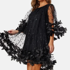 Svart klänning från Ida Sjöstedt - Säljer en fantastisk svart klänning från Ida Sjöstedt med glittriga detaljer och volanger. Klänningen har trekvartsärmar och är dekorerad med vackra blommor. Perfekt för en speciell kväll! ✨