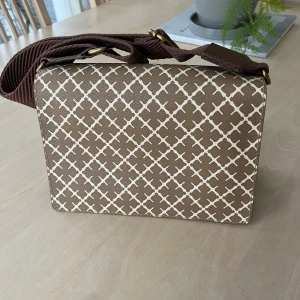 BY MALENE BIRGER - AXELREMSVÄSKA LOENNA - Snygg brun axelväska med ett stilrent rutigt mönster i vitt. Väskan har en justerbar axelrem och flera fack inuti för enkel organisering.  