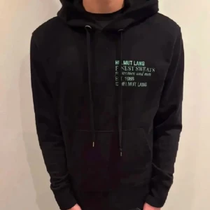 Svart hoodie från Helmut Lang - Säljer en svart hoodie från Helmut Lang med tryck på bröstet. Den har en klassisk design med dragsko i huvan och en stor ficka framtill. Perfekt för en stilren och bekväm look.Tyvärr var den för stor för min son. Stl XS men skulle mer säga M då den är stor i stl. Personen på bilden är 176 cm.. Bra skick!