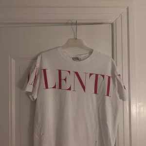 Vit t-shirt med röd text från Valentino - Snygg vit t-shirt från Valentino med stor röd text på framsidan. Den har en klassisk rund hals och korta ärmar. Perfekt för en stilren och trendig look.