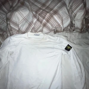 Vit Stone Island tröja - Säljer en stilren vit långärmad tröja från Stone Island. Tröjan har en klassisk design med det ikoniska Stone Island-märket på ärmen. Perfekt för en avslappnad och trendig look.