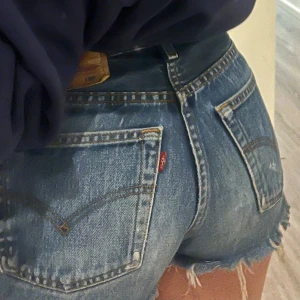 Blå jeansshorts från Levi's - Snygga blå jeansshorts från Levi's med fransiga kanter och slitna detaljer.  Levi's ikoniska lädermärke baktill. 