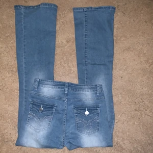 Blå utsvängda jeans med broderade bakfickor - Snygga blå utsvängda jeans med broderade detaljer på bakfickorna och knappar. Perfekta för en avslappnad stil med en klassisk look.