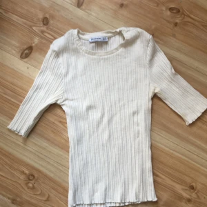 Vit ribbad topp från Stradivarius - Säljer en stilren vit ribbad topp från Stradivarius. Toppen har trekvartsärmar och en rund halsringning, perfekt för en avslappnad look. Tillverkad i Turkiet och passar bra till både jeans och kjol. Perfekt för vår och sommar!