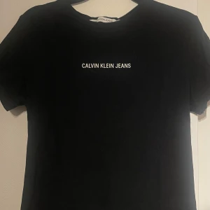 Svart t-shirt från Calvin Klein Jeans - Snygg svart t-shirt från Calvin Klein Jeans med vit logga på bröstet. Perfekt för en stilren och enkel look. T-shirten har en klassisk passform och är kortärmad.
