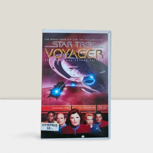 Star Trek Voyager 5.2 - Extreme Risk/In the Flesh VHS-STVOY - Säljer en begagnad VHS-kassett av Star Trek Voyager med avsnitten 'Extreme Risk' och 'In the Flesh'. Omslaget har en futuristisk design med rymdskepp och karaktärer från serien. Perfekt för samlare eller nostalgiker som älskar klassisk sci-fi.