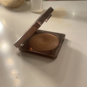 Bronzer från CAIA - Snygg bronzer från CAIA i nyansen 'La Digue'. Kompakt förpackning med spegel, perfekt för att ge ansiktet en solkysst look. Säljer pågrund av färgen, den är för ljus för mig. Använde som ögonskugga. 