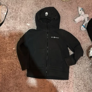 Svart hoodie från Sail Racing - Säljer en svart hoodie från Sail Racing med dragkedja och huva. Den har två fickor framtill och en stilren logga på bröstet. Perfekt för en avslappnad stil. Ord pris 1100 typ lite sålbränd så säljer ganska billigt 