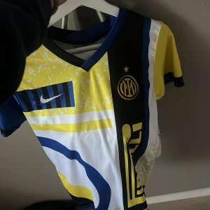 Inter Milan fotbollströja med nummer 9 - Säljer en unik Inter Milan fotbollströja från Nike med ett färgglatt och iögonfallande mönster. Tröjan har korta ärmar och är designad i färgerna gul, blå, svart och vit. Den har nummer 9 på ryggen och klubbens emblem på framsidan.