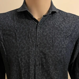 Mörkblå paisleymönstrad skjorta från Castor Pollux - Snygg mörkblå skjorta från Castor med paisleymönster. Skjortan har långa ärmar och knappar framtill. Perfekt för en stilren look.