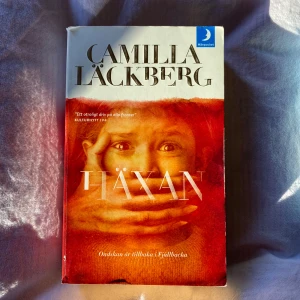 Häxan - Pocketbok av Camilla Läckberg, del av Fjällbackaserien. Omslaget är rött med en bild av ett barn och titeln 'Häxan' i stora bokstäver. Boken handlar om ett mysterium i Fjällbacka där en flicka försvinner, vilket väcker minnen av ett tidigare fall.