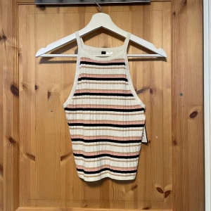 Oanvänd randig ribbad linnetopp från H&M - Säljer en snygg randig linnetopp från H&M i vitt, svart och rosa. Toppen är ribbad och har smala axelband, perfekt för varma dagar. Passar bra till både jeans och kjol.