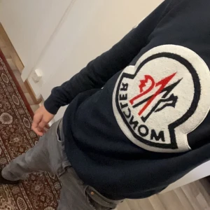 Mörkblå moncler sweatshirt äkta  - Säljer en svart tröja med en stor, iögonfallande logotyp på framsidan. Tröjan har långa ärmar och en bekväm passform. Perfekt för en avslappnad stil. 