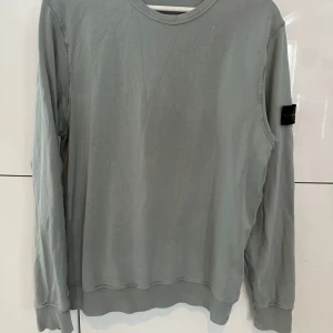 Grå långärmad tröja från Stone Island - Säljer en stilren grå långärmad tröja från Stone Island. Tröjan har en rund halsringning och det ikoniska Stone Island-märket på ärmen. Perfekt för en avslappnad och trendig look som är köpt på ni i Sthlm.