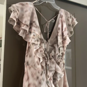Mönstrad klänning från Rotate - Säljer en snygg klänning från Rotate med volanger och djup v-ringning. Klänningen har ett unikt mönster i ljusa toner och knytband i ryggen. Perfekt för en somrig look!