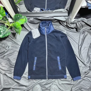 Moncler cardigan - Säljer en snygg mörkblå fleecejacka från Moncler. Den har en quiltad krage och dragkedja framtill. Jackan är i nyskick och perfekt för höst och vår. Den har också snygga detaljer med knappar på fickorna. Perfekt för dig som vill ha både stil och komfort! Extremt unik och extremt snygg