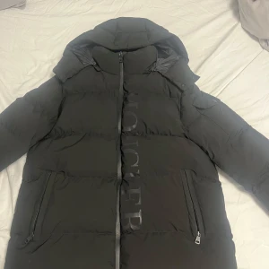 Moncler Jacka - Svart Moncler jacka i storlek L men passar även M och XL. Användes endast 1 gång. Extremt bekväm och varmt. Den här även avtagbar luva och en vattentät innerficka. Säljer den eftersom jag inte använder den alls.