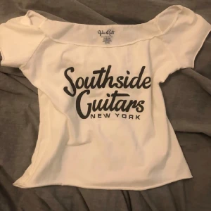Brandy Melville topp - Säljer en snygg vit t-shirt från John Galt (brandy Melville) med trycket 'Southside Guitars New York' i svart. Perfekt för en avslappnad stil och passar till allt! T-shirten är kortärmad och gjord i mjuk bomull. Köpte I London typ 2 månader sen