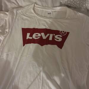 Säljer en klassisk vit t-shirt från Levi's med deras ikoniska röda logga på bröstet. Perfekt för en avslappnad stil och passar till allt. T-shirten är i bomull och har en normal passform. Perfekt för både vardag och fest!