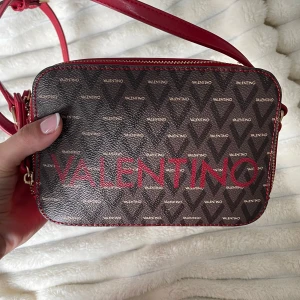 Valentino liuto across body bag  - Jättefin valentino väska som används vid ett tillfälle. Alltså splitterny! Färgen i denna modell säljs ej längre. Inköpspris ca. 1000kr. Medföljande påse skickas med!   Har förvarats bra och har felfri form. Kommer självklart postas i en kartong!