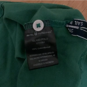 Grön polo från Sail Racing - Säljer en snygg grön polo från Sail Racing i storlek medium. Den är gjord av 100% bomull och har en klassisk krage med knappar. På framsidan finns ett tryck med siffran 77 och Sail Racing-loggan. Perfekt för en avslappnad stil!