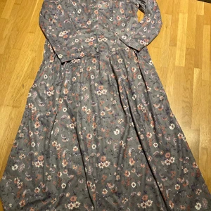 Klänning från wästgöta - Lång blommig klänning med axelvaddar Och knytband i ryggen  Armarna ser inte hellånga ut  Strl 20, vet inte vad det motsvarar