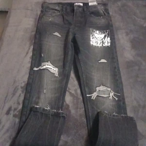 Svarta jeans med tryck och slitningar från FSBN - Säljer ett par svarta jeans från FSBN med coola slitningar och ett tryck på ena benet. Har aldrig använt den.